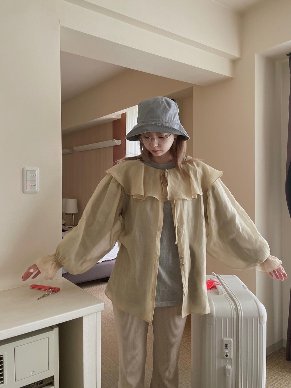 ベージュ系のシャツ/ブラウス、ベージュ系のスニーカー、ホワイト系のスーツケース/キャリーバッグを着用したレディースの春コーディネートの3枚目の写真