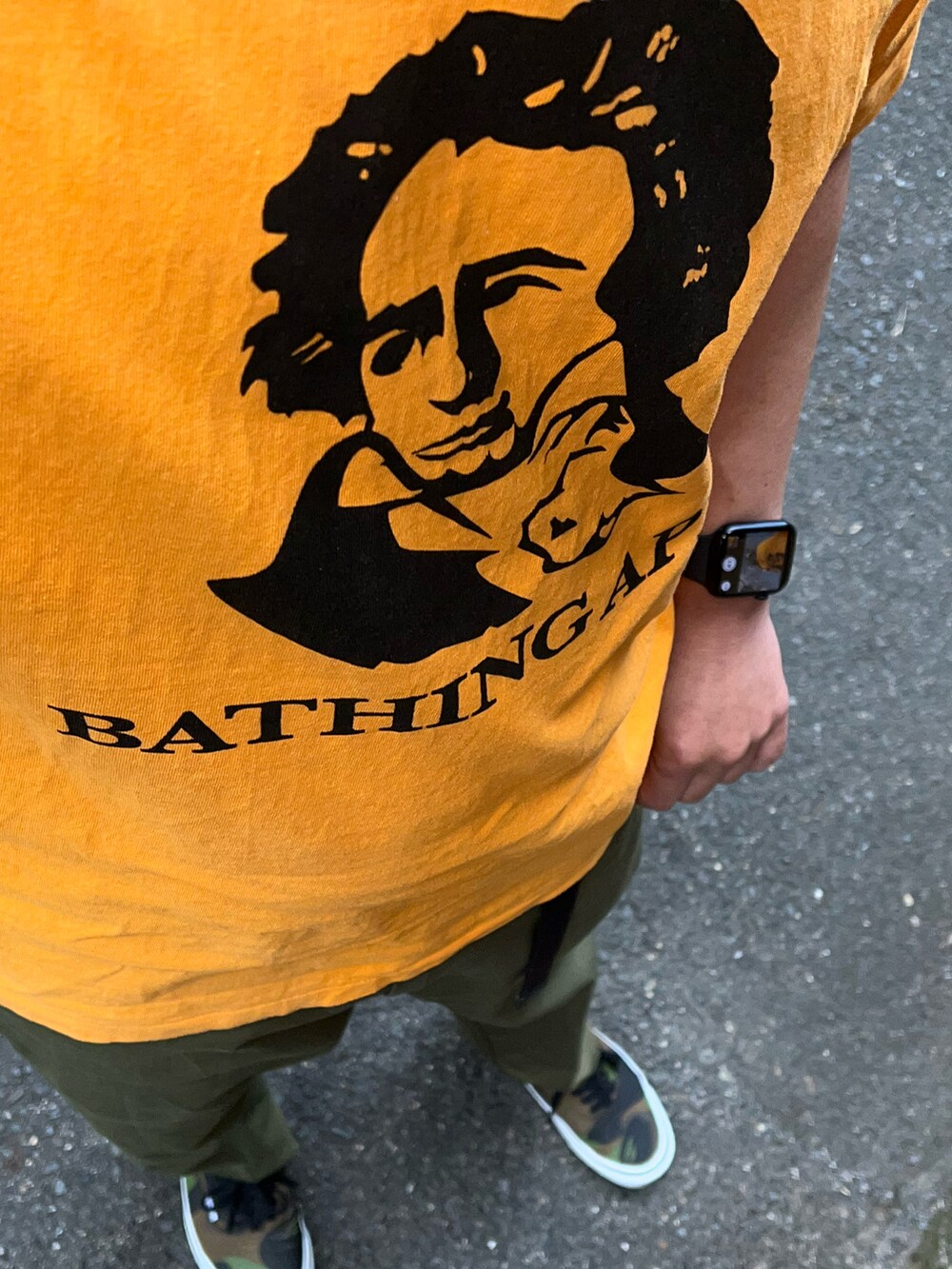 グリーン系のチノパンツ、グリーン系のスニーカー、オレンジ系のTシャツ/カットソーを着用したメンズの夏コーディネートの3枚目の写真