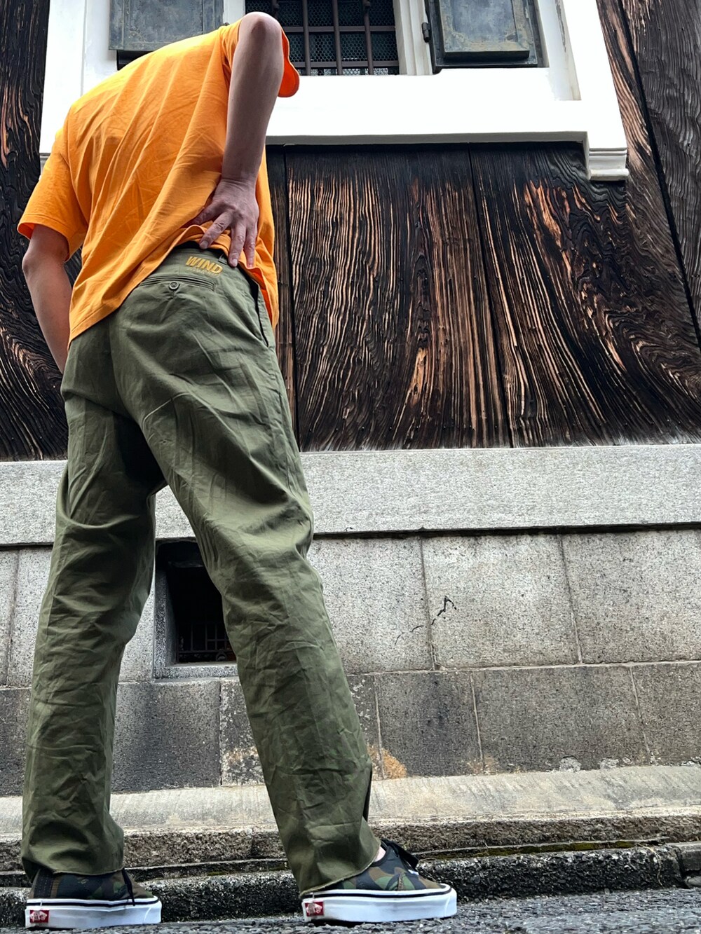 グリーン系のチノパンツ、グリーン系のスニーカー、オレンジ系のTシャツ/カットソーを着用したメンズの夏コーディネートの2枚目の写真