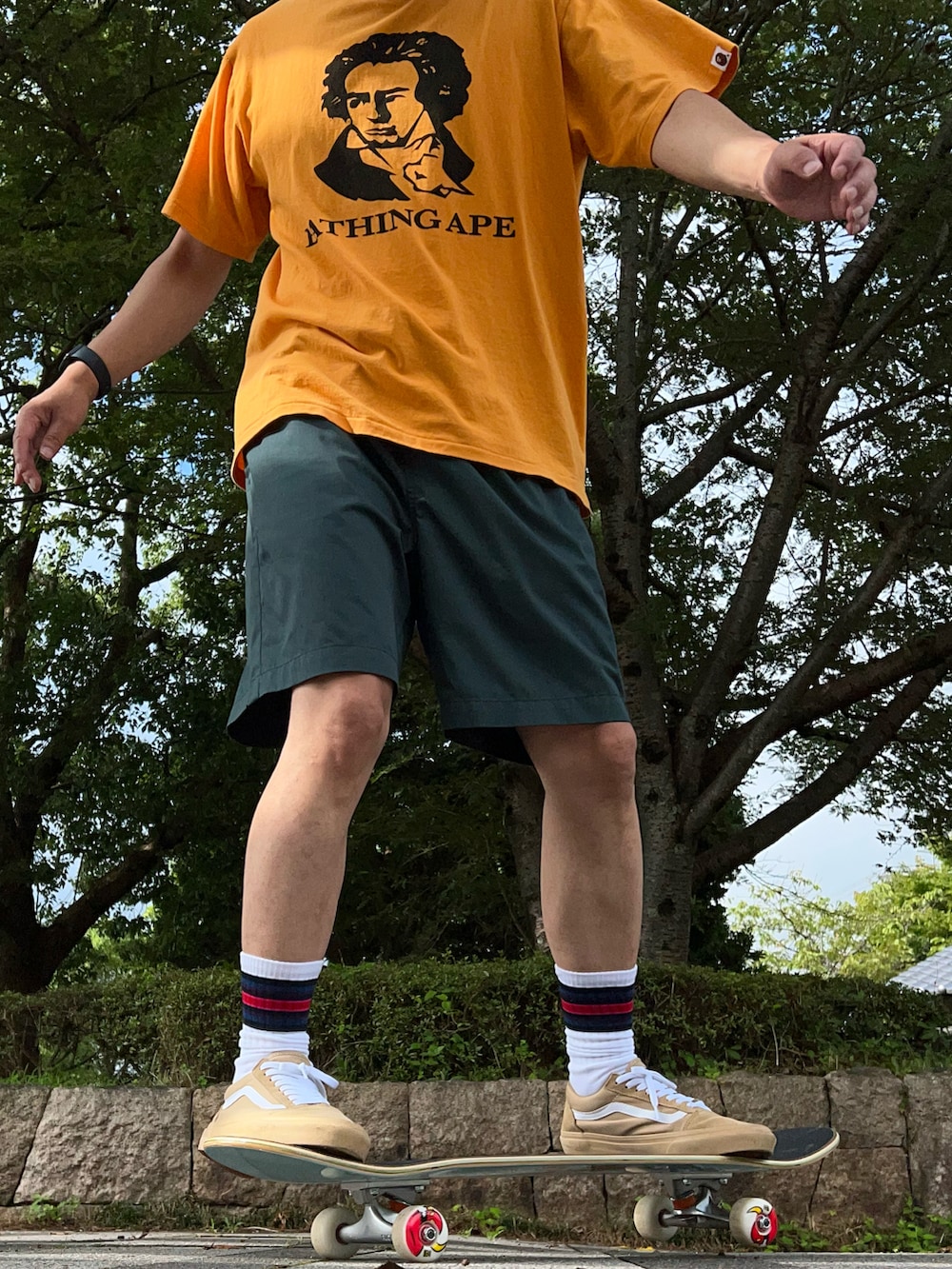 オレンジ系のTシャツ/カットソー、グリーン系のチノパンツ、ベージュ系のスニーカーを着用したメンズの夏コーディネートの3枚目の写真