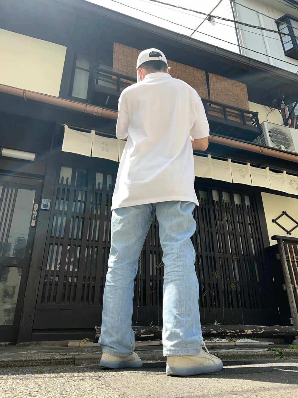 ブルー系のデニムパンツ、ベージュ系のスニーカー、ホワイト系のポロシャツを着用したメンズの春コーディネートの2枚目の写真