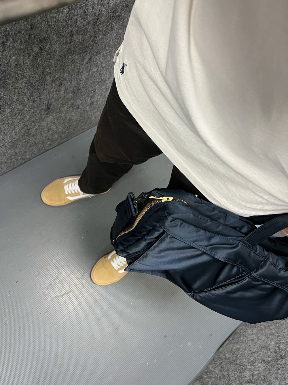 ホワイト系のポロシャツ、グレー系のチノパンツ、ブルー系のビジネスバッグを着用したメンズの夏コーディネートの3枚目の写真