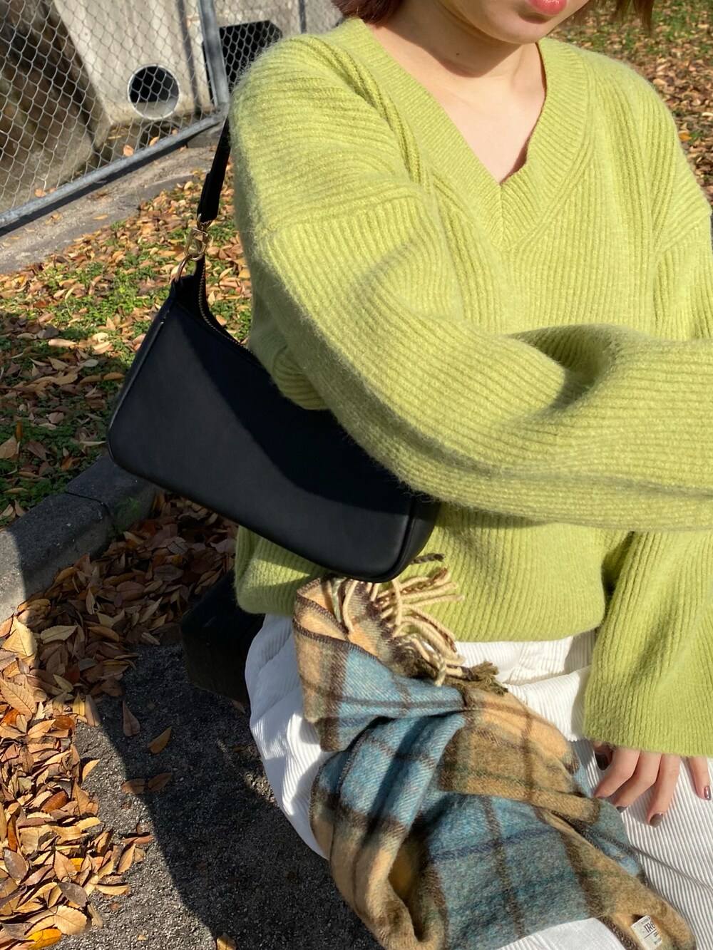 グリーン系のトップス、ブラック系のバッグ、ホワイト系のパンツを着用したレディースの秋コーディネートの4枚目の写真