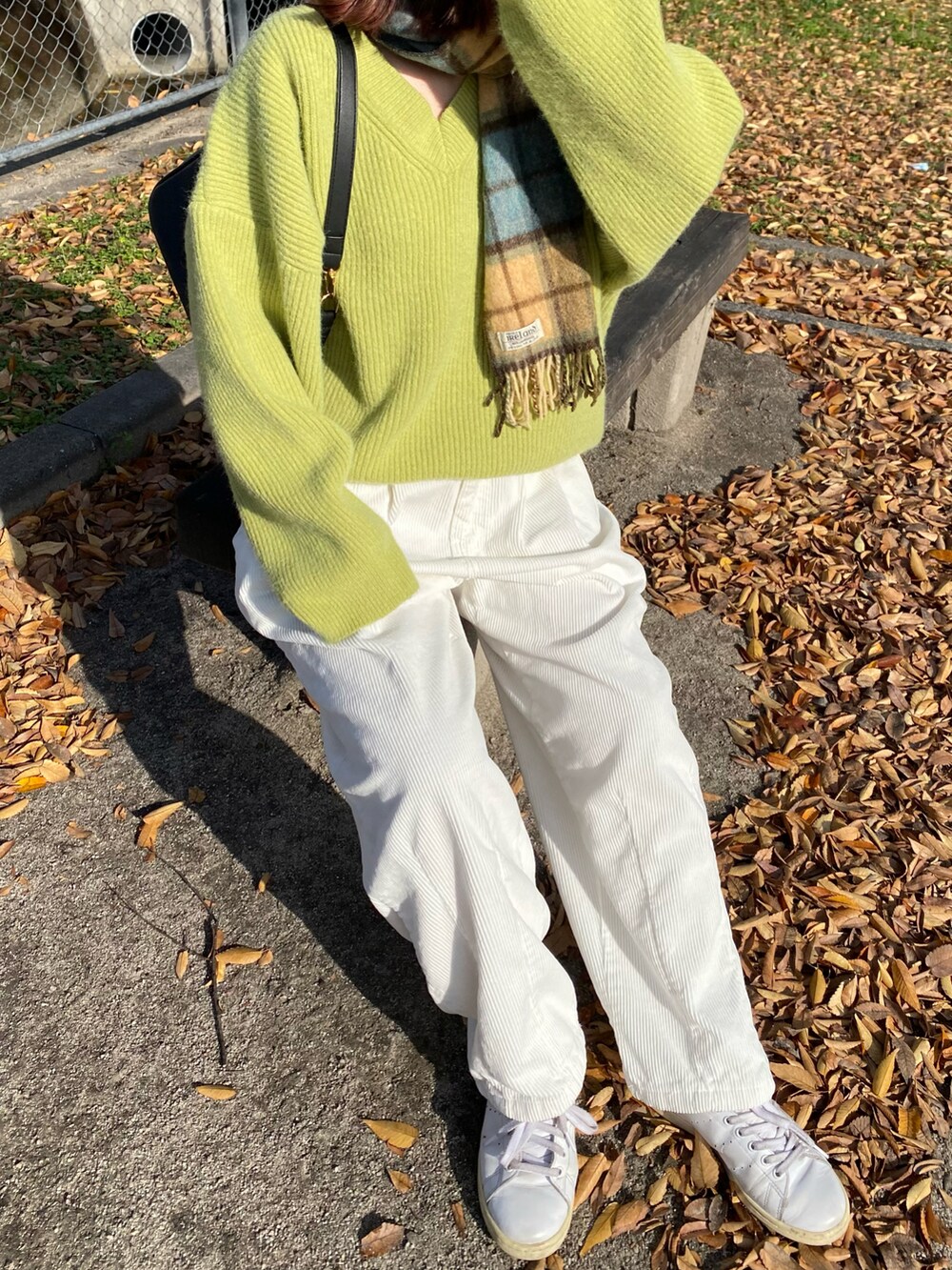 グリーン系のトップス、ブラック系のバッグ、ホワイト系のパンツを着用したレディースの秋コーディネートの3枚目の写真