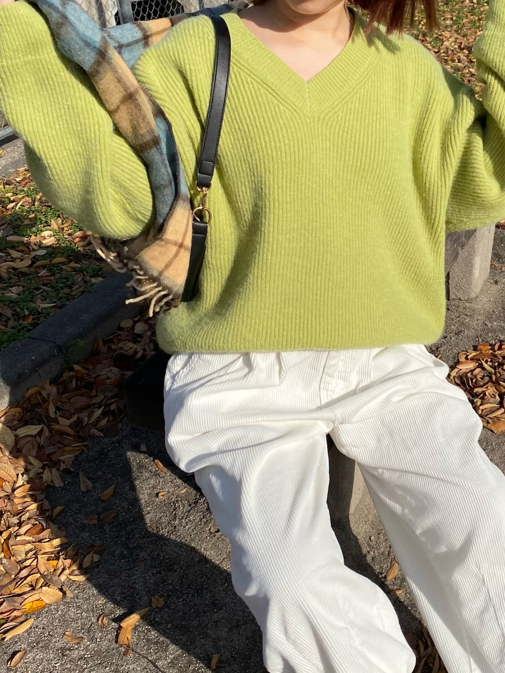 グリーン系のトップス、ブラック系のバッグ、ホワイト系のパンツを着用したレディースの秋コーディネートの2枚目の写真