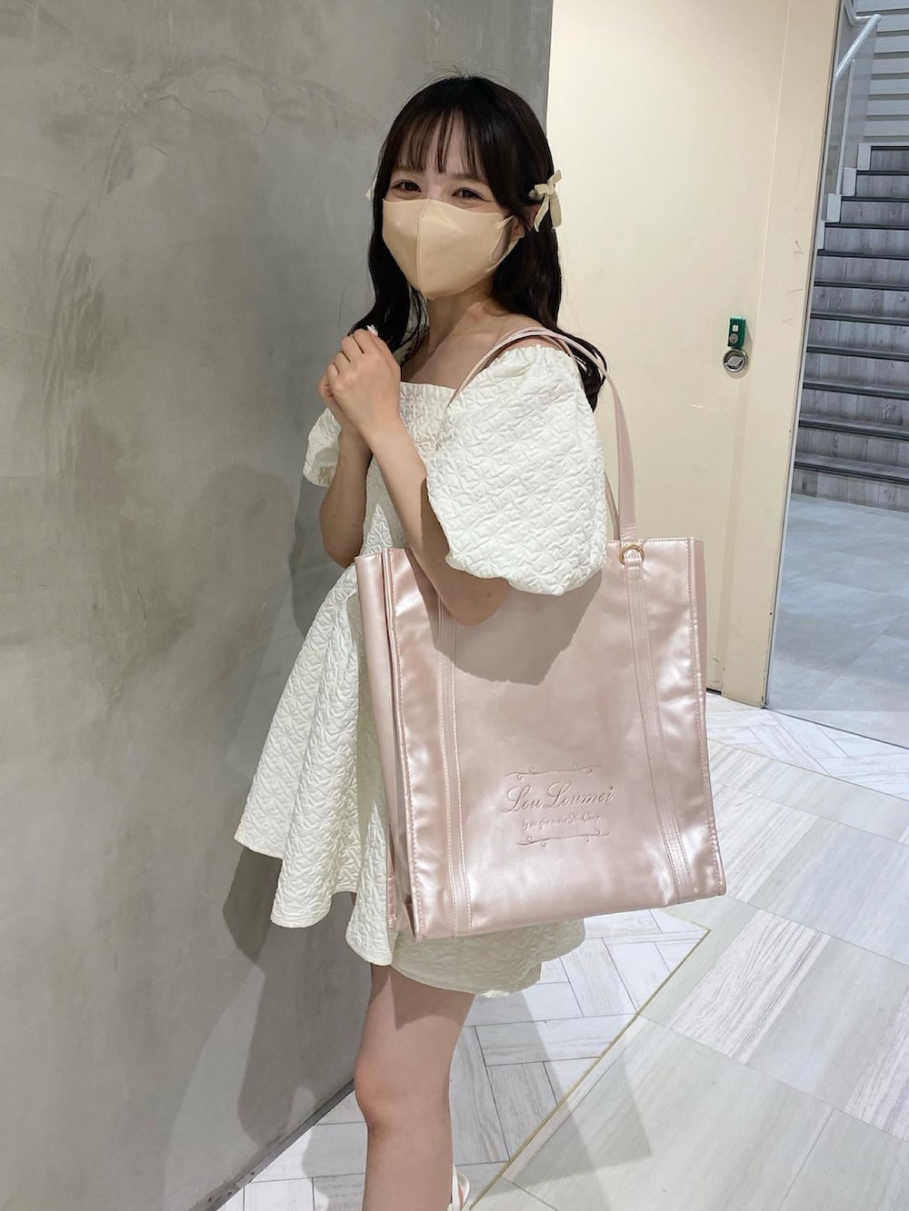 ピンク系のトートバッグ、ホワイト系のチュニックを着用したレディースの夏コーディネートの2枚目の写真