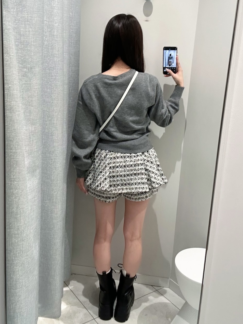 グレー系のニット/セーター、ブラック系のスカート、ホワイト系のショルダーバッグを着用したレディースの秋コーディネートの5枚目の写真