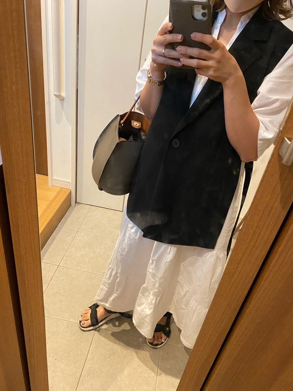 ブラック系のベスト、ホワイト系のシャツワンピース、ブラック系のサンダルを着用したレディースの夏コーディネートの2枚目の写真