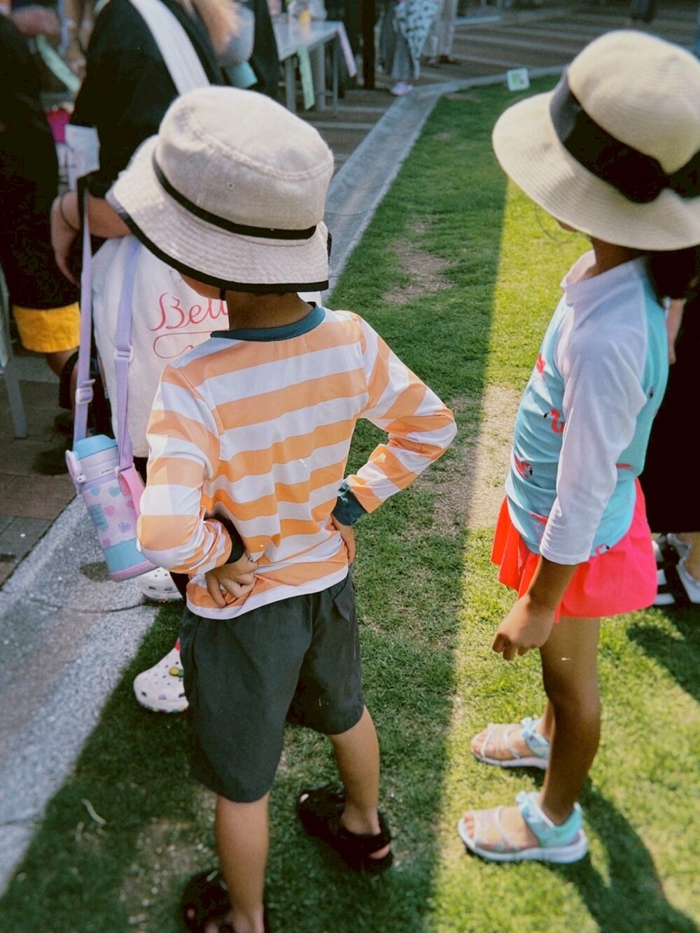 ブラック系のサンダル、グレー系のパンツ、オレンジ系のラッシュガードを着用したキッズの夏コーディネートの3枚目の写真