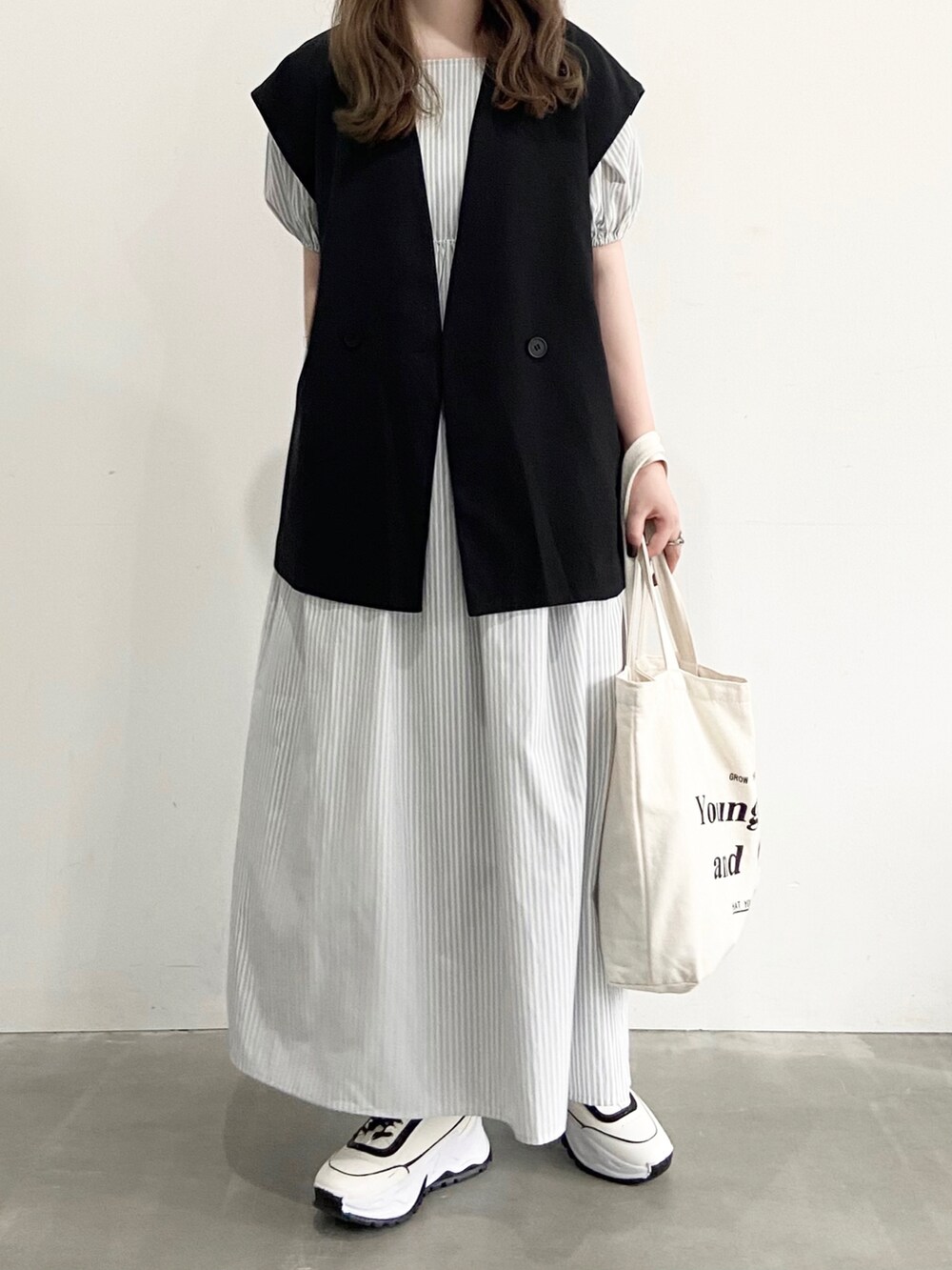 ホワイト系のスニーカー、グレー系のワンピース、ブラック系のベストを着用したレディースの夏コーディネートの2枚目の写真