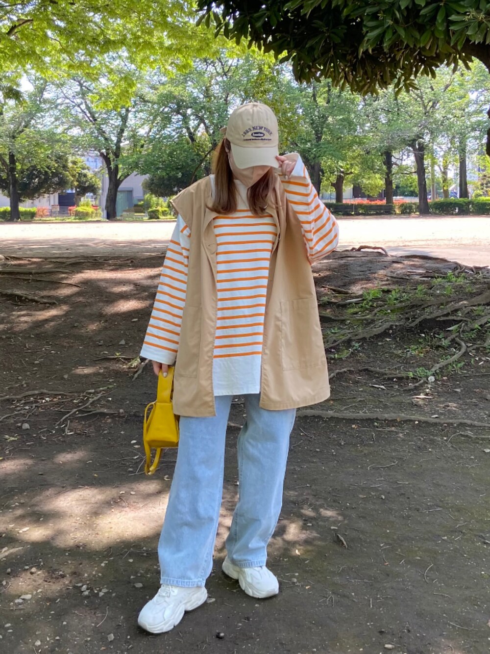 ベージュ系のスニーカー、オレンジ系のTシャツ/カットソー、ベージュ系のステンカラーコートを着用したレディースの春コーディネートの2枚目の写真