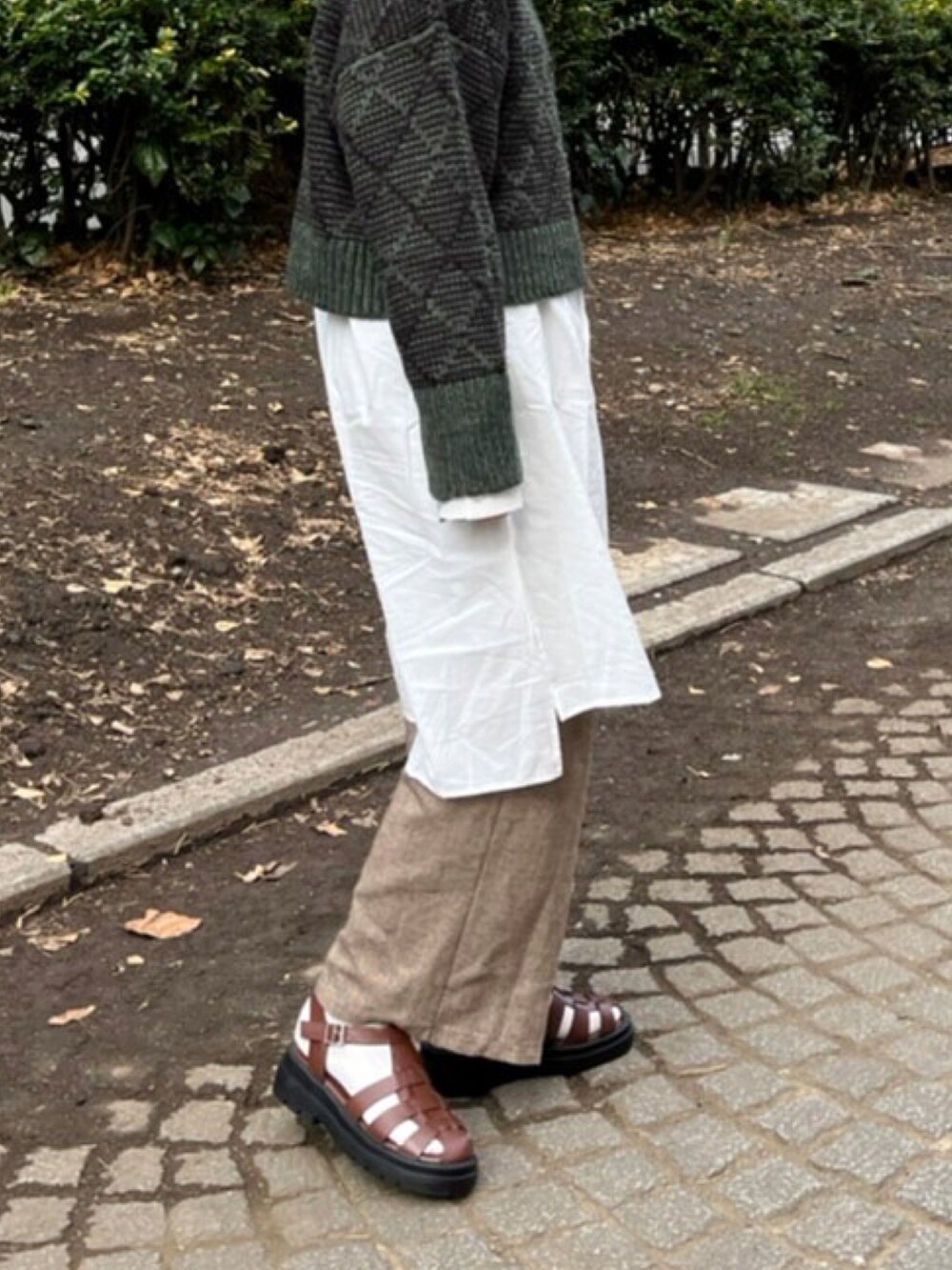 グリーン系のニット/セーター、ホワイト系のシャツ/ブラウス、ブラウン系のサンダルを着用したレディースの冬コーディネートの2枚目の写真
