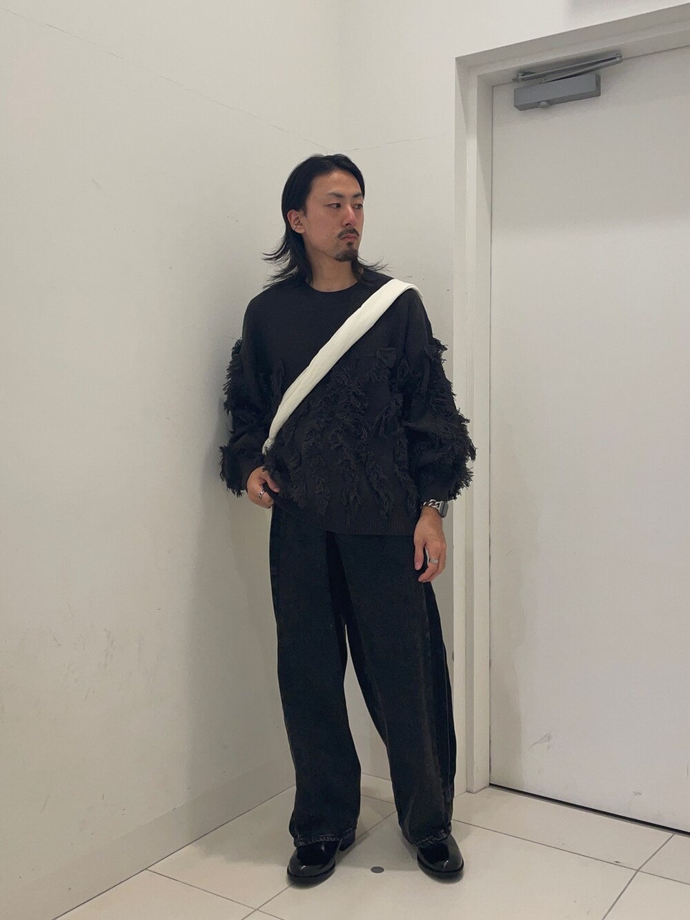 ブラック系のデニムパンツ、グレー系のニット/セーター、ホワイト系のショルダーバッグを着用したメンズの秋コーディネートの2枚目の写真
