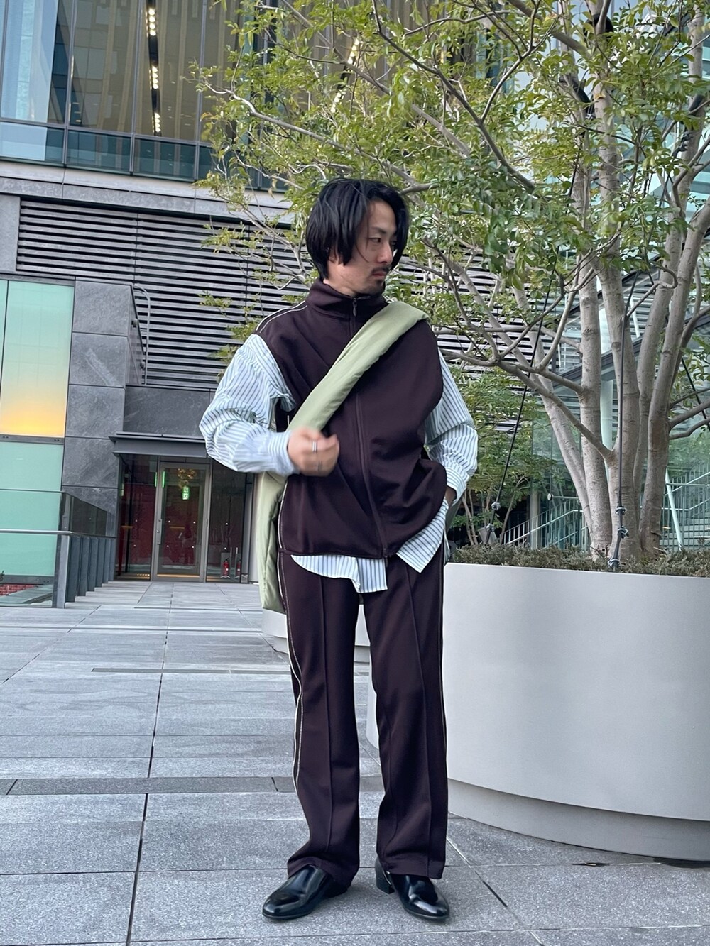 ブラウン系のその他パンツ、ブラウン系のベスト、グリーン系のショルダーバッグを着用したメンズの春コーディネートの2枚目の写真