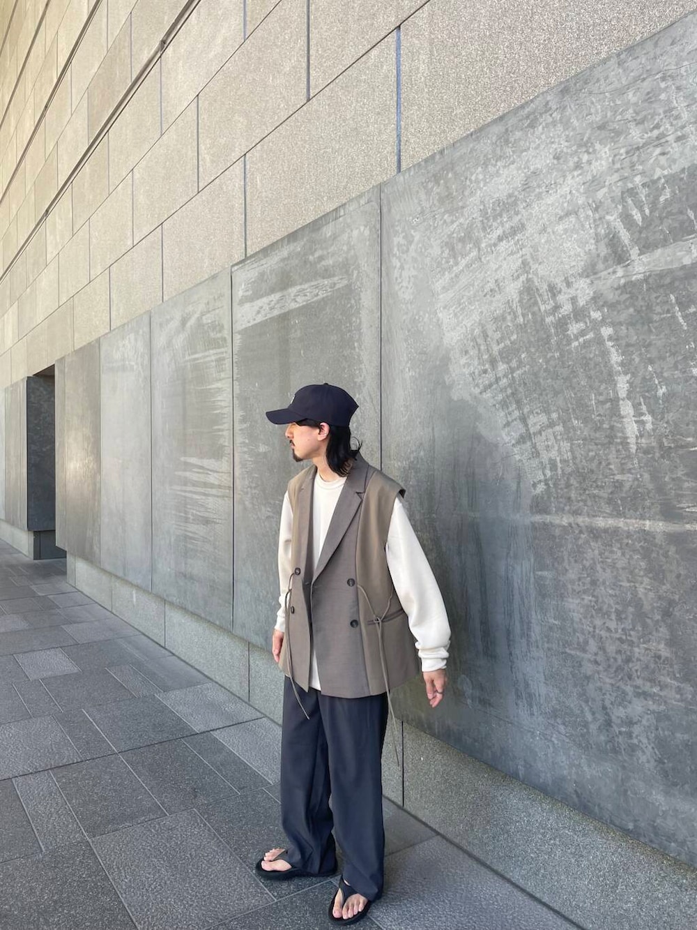 グレー系のスラックス、ブラウン系のベスト、ブルー系のキャップを着用したメンズの夏コーディネートの3枚目の写真