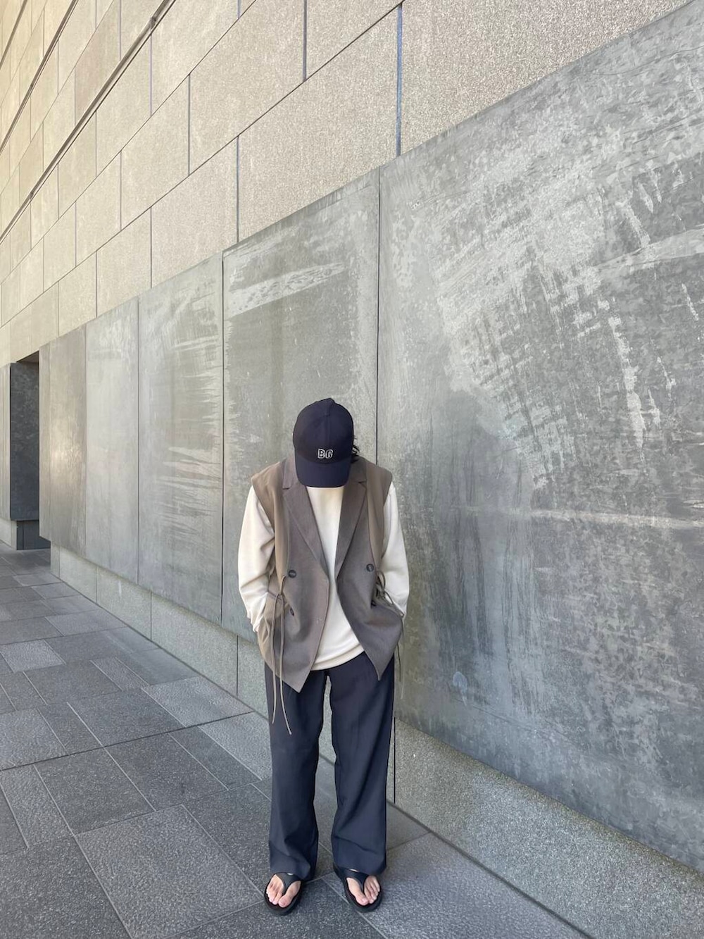 グレー系のスラックス、ブラウン系のベスト、ブルー系のキャップを着用したメンズの夏コーディネートの2枚目の写真