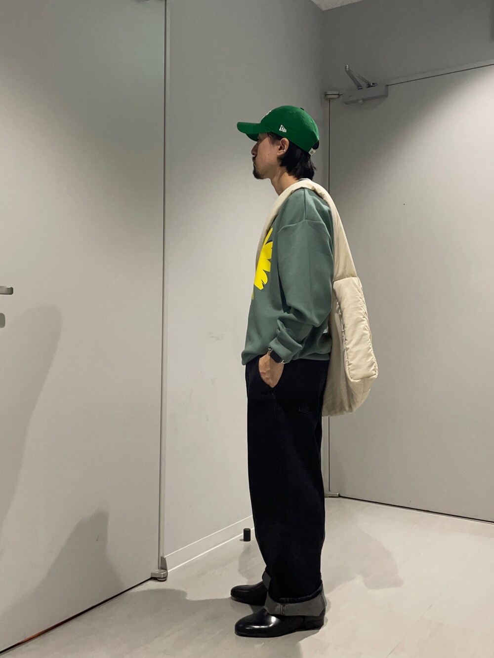 グリーン系のスウェット、ブラック系のデニムパンツ、グリーン系のショルダーバッグを着用したメンズの春コーディネートの2枚目の写真