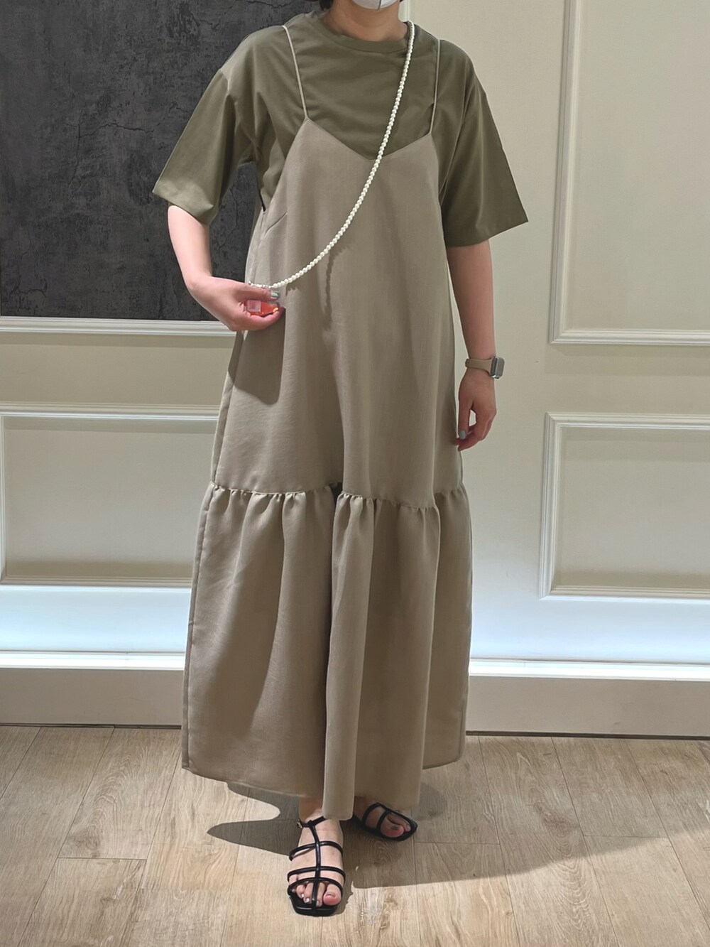 ベージュ系のワンピース、グリーン系のTシャツ/カットソー、ブラック系のサンダルを着用したレディースの春コーディネートの2枚目の写真