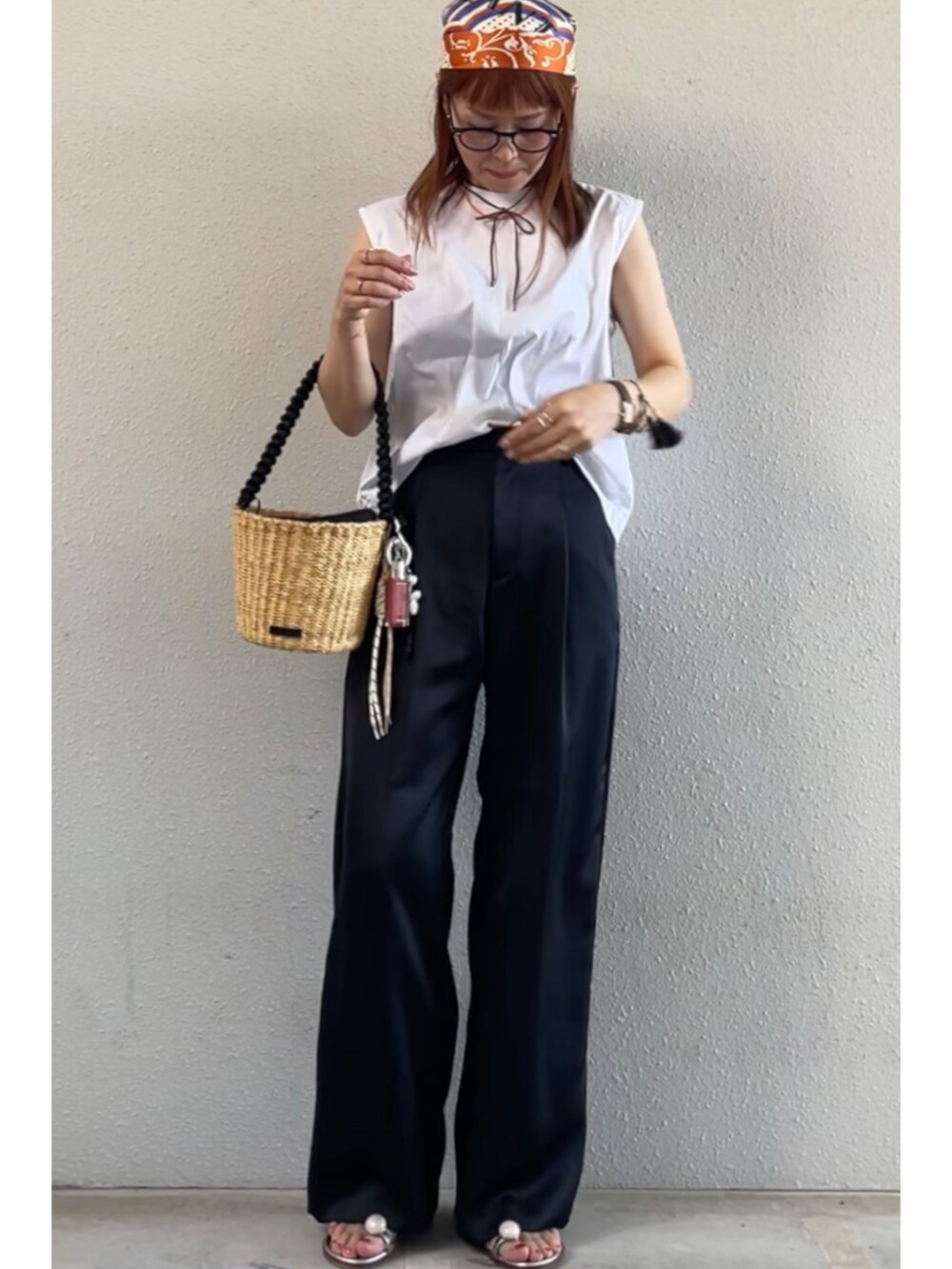 ブルー系のスラックス、ブラック系のかごバッグ、オレンジ系のバンダナ/スカーフを着用したレディースの夏コーディネートの2枚目の写真