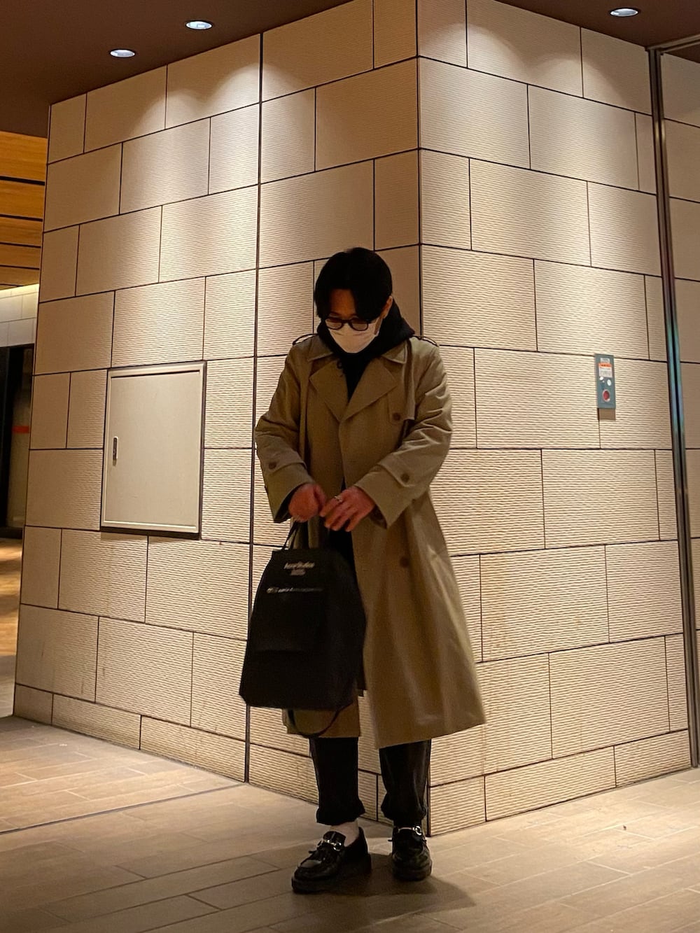 ブラック系のパーカー、ブラック系のローファー、ベージュ系のトレンチコートを着用したメンズの冬コーディネートの4枚目の写真