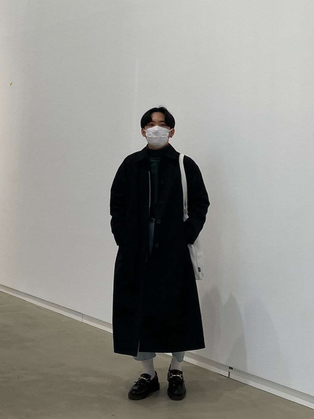 ブラック系のステンカラーコート、グリーン系のスウェット、ホワイト系のトートバッグを着用したメンズの春コーディネートの5枚目の写真