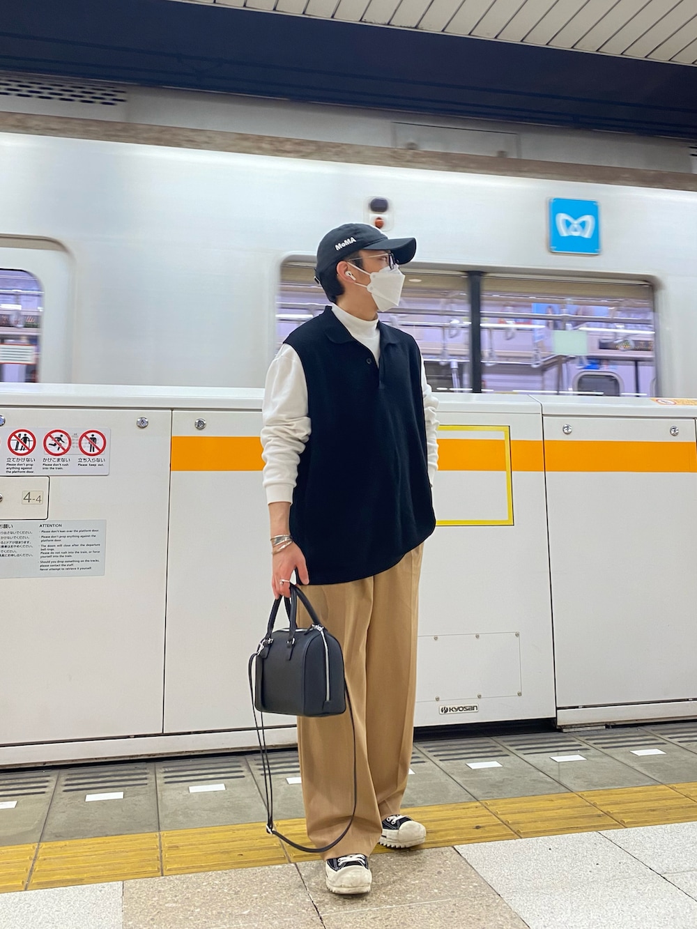 ブラック系のベスト、ホワイト系のTシャツ/カットソー、ベージュ系のスラックスを着用したメンズの春コーディネートの2枚目の写真