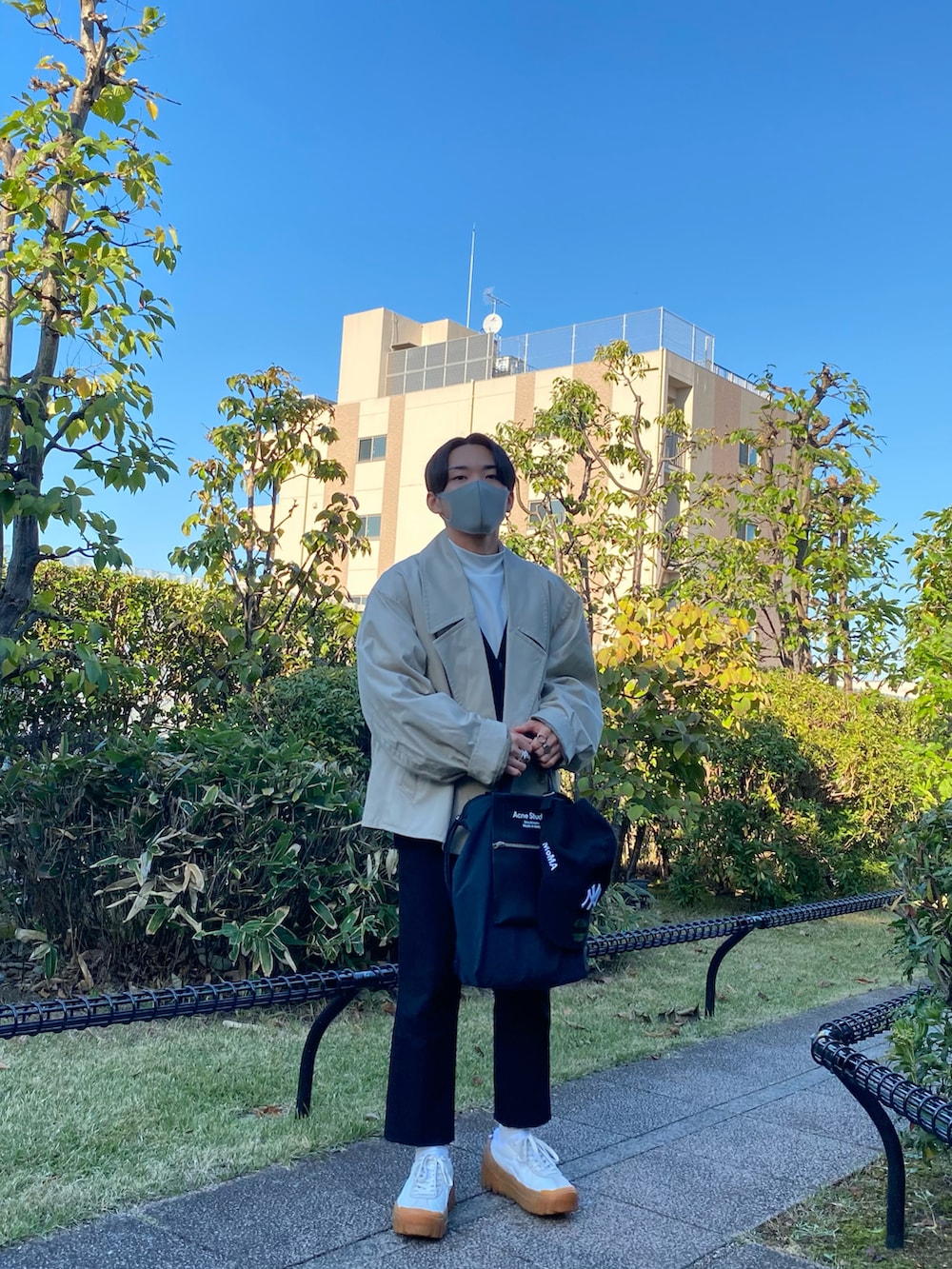 ベージュ系のトレンチコート、ブラック系のカーディガン/ボレロ、ホワイト系のTシャツ/カットソーを着用したメンズの秋コーディネートの2枚目の写真