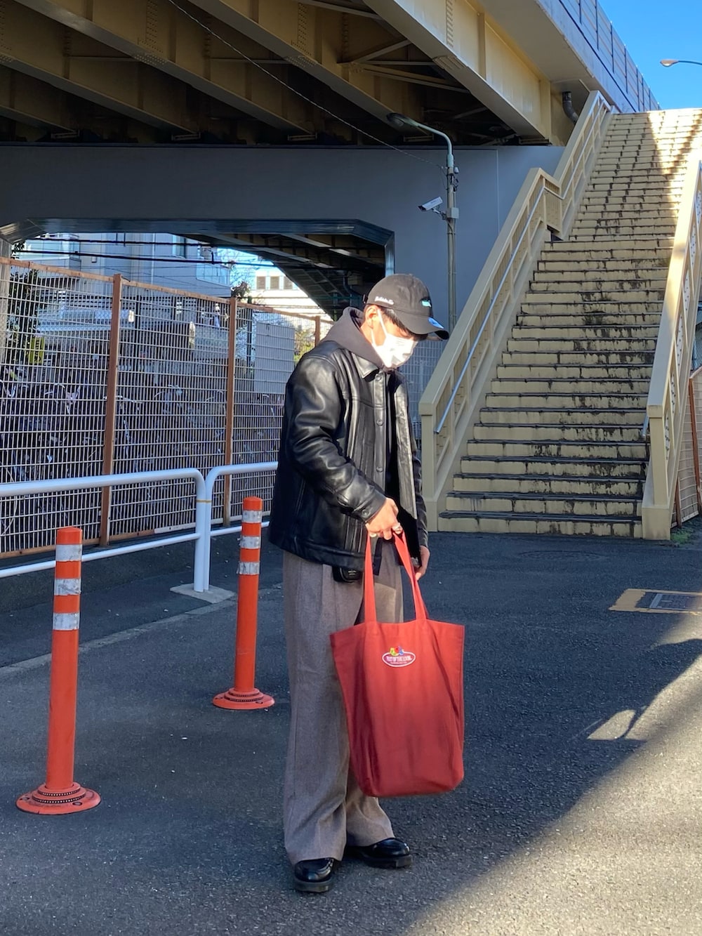 ブラック系のライダースジャケット、ブラック系のパーカー、レッド系のトートバッグを着用したメンズの秋コーディネートの5枚目の写真