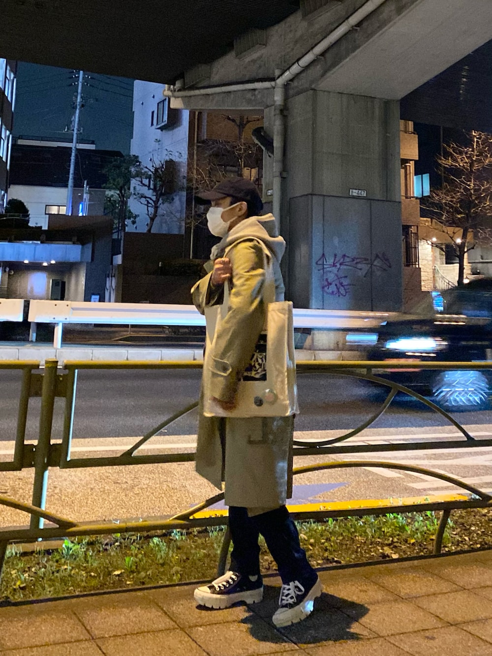 ベージュ系のトレンチコート、グレー系のパーカー、ホワイト系のトートバッグを着用したメンズの春コーディネートの2枚目の写真