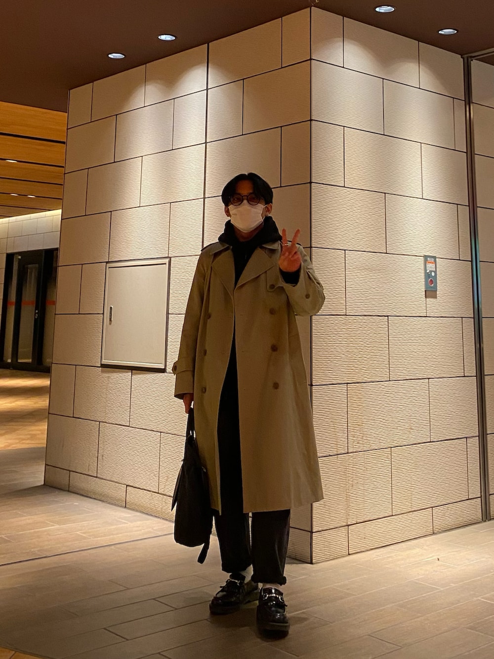 ブラック系のパーカー、ブラック系のローファー、ベージュ系のトレンチコートを着用したメンズの冬コーディネートの2枚目の写真