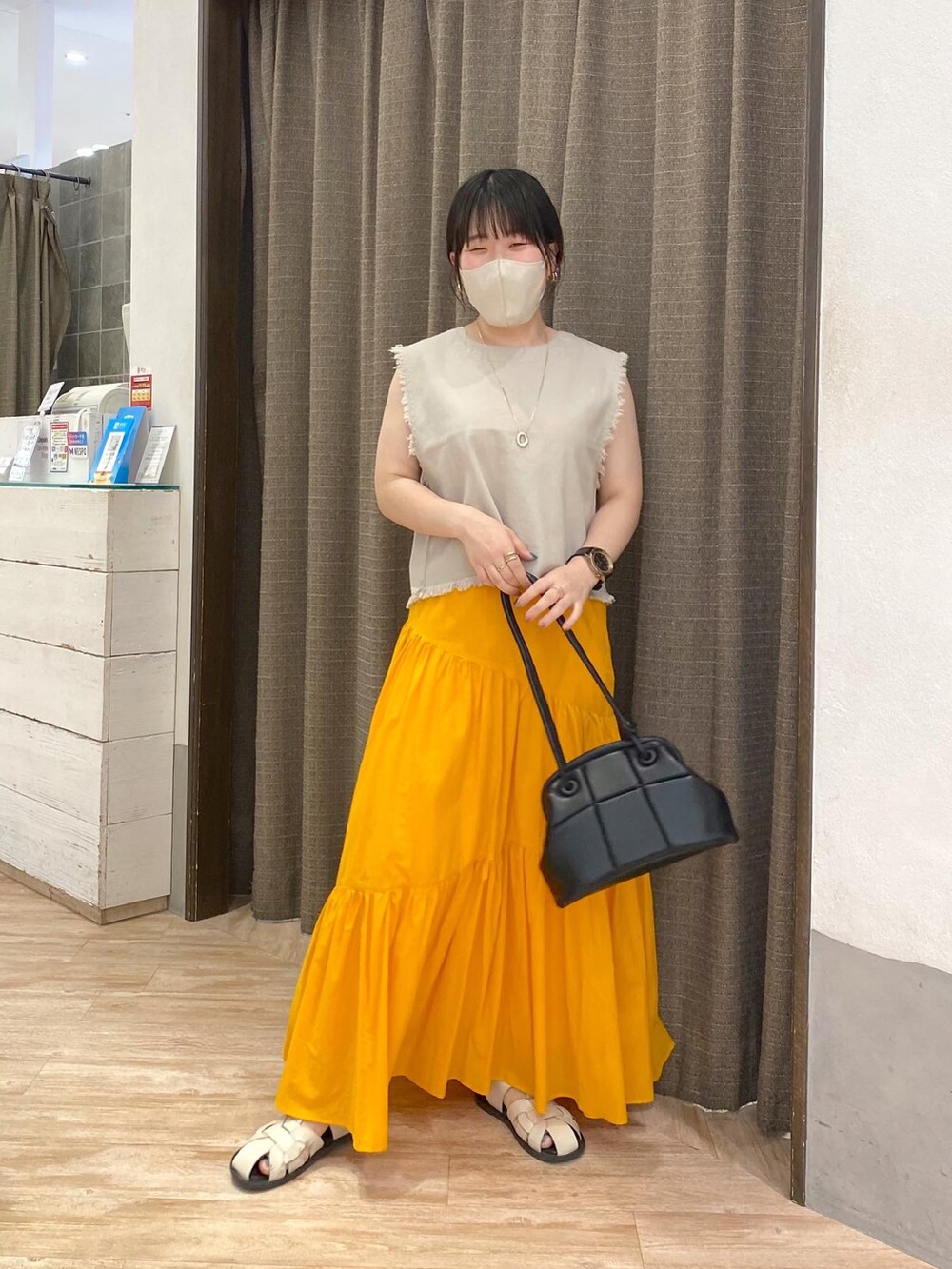 ホワイト系のベスト、オレンジ系のスカート、ホワイト系のサンダルを着用したレディースの夏コーディネートの2枚目の写真