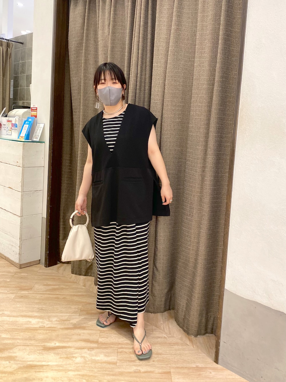 ブラック系のベスト、ホワイト系のワンピース、グリーン系のその他シューズを着用したレディースの夏コーディネートの2枚目の写真