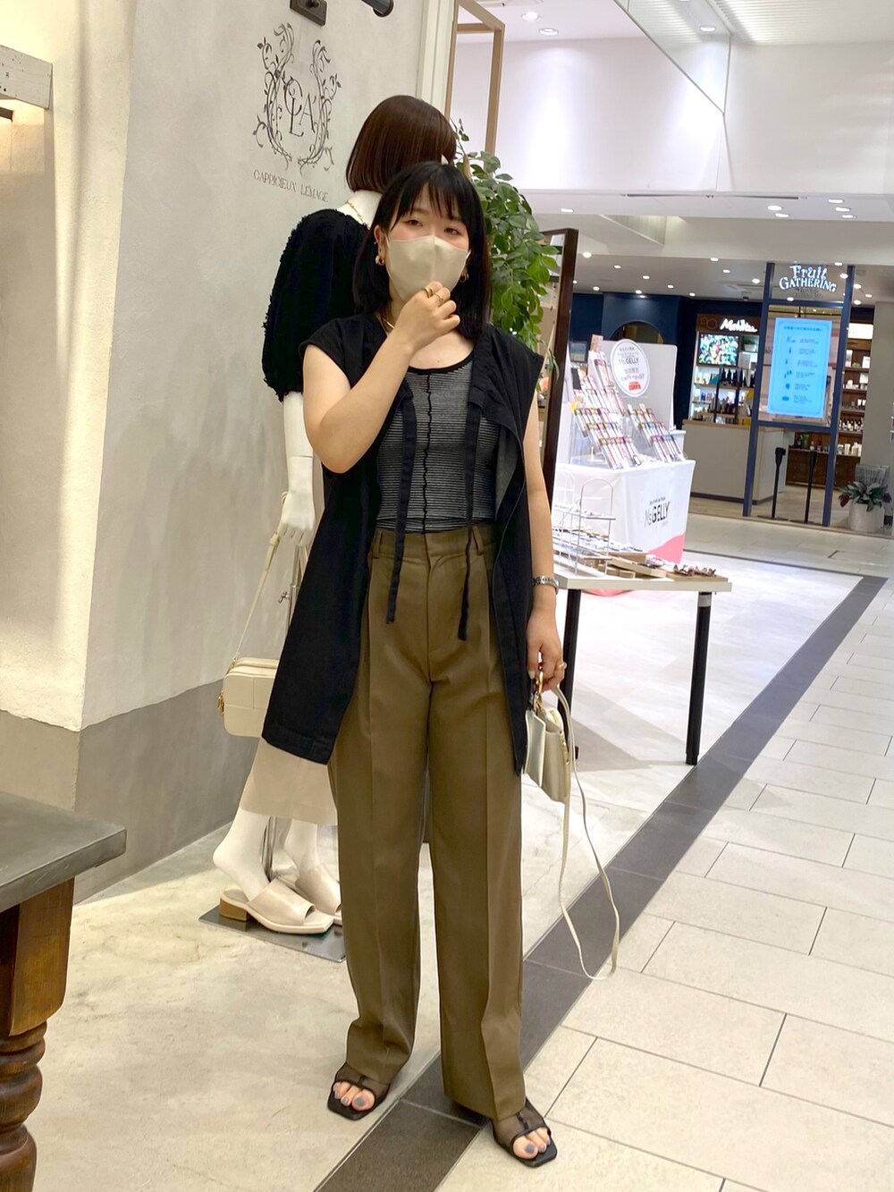 ブラック系のベスト、ブラウン系のスラックス、ホワイト系のショルダーバッグを着用したレディースの夏コーディネートの2枚目の写真