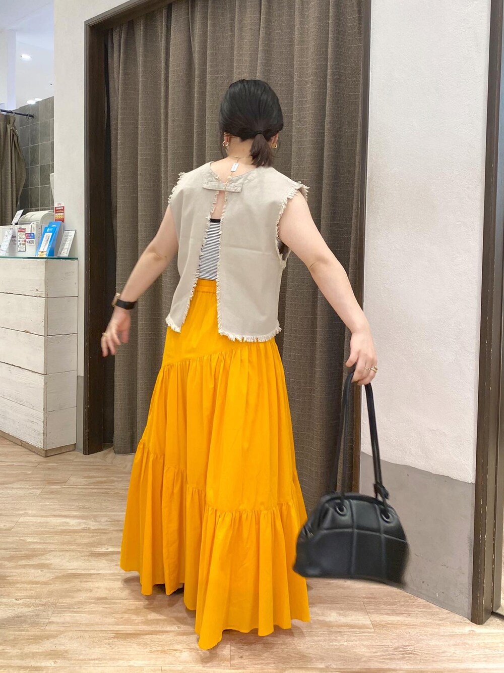 ホワイト系のベスト、オレンジ系のスカート、ホワイト系のサンダルを着用したレディースの夏コーディネートの3枚目の写真