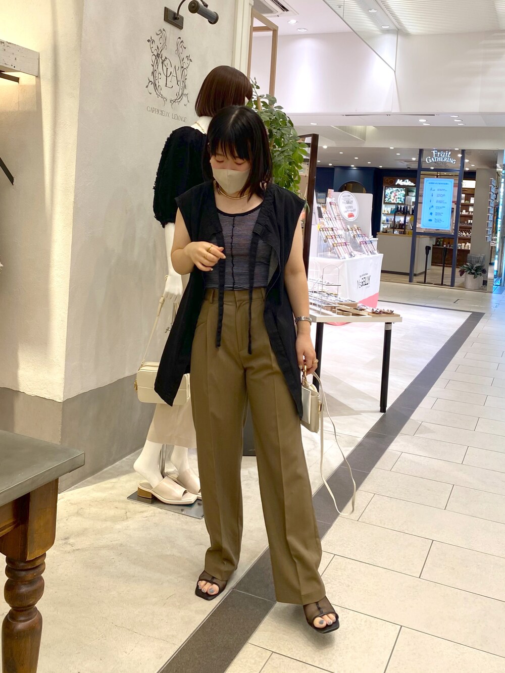 ブラック系のベスト、ブラウン系のスラックス、ホワイト系のショルダーバッグを着用したレディースの夏コーディネートの3枚目の写真