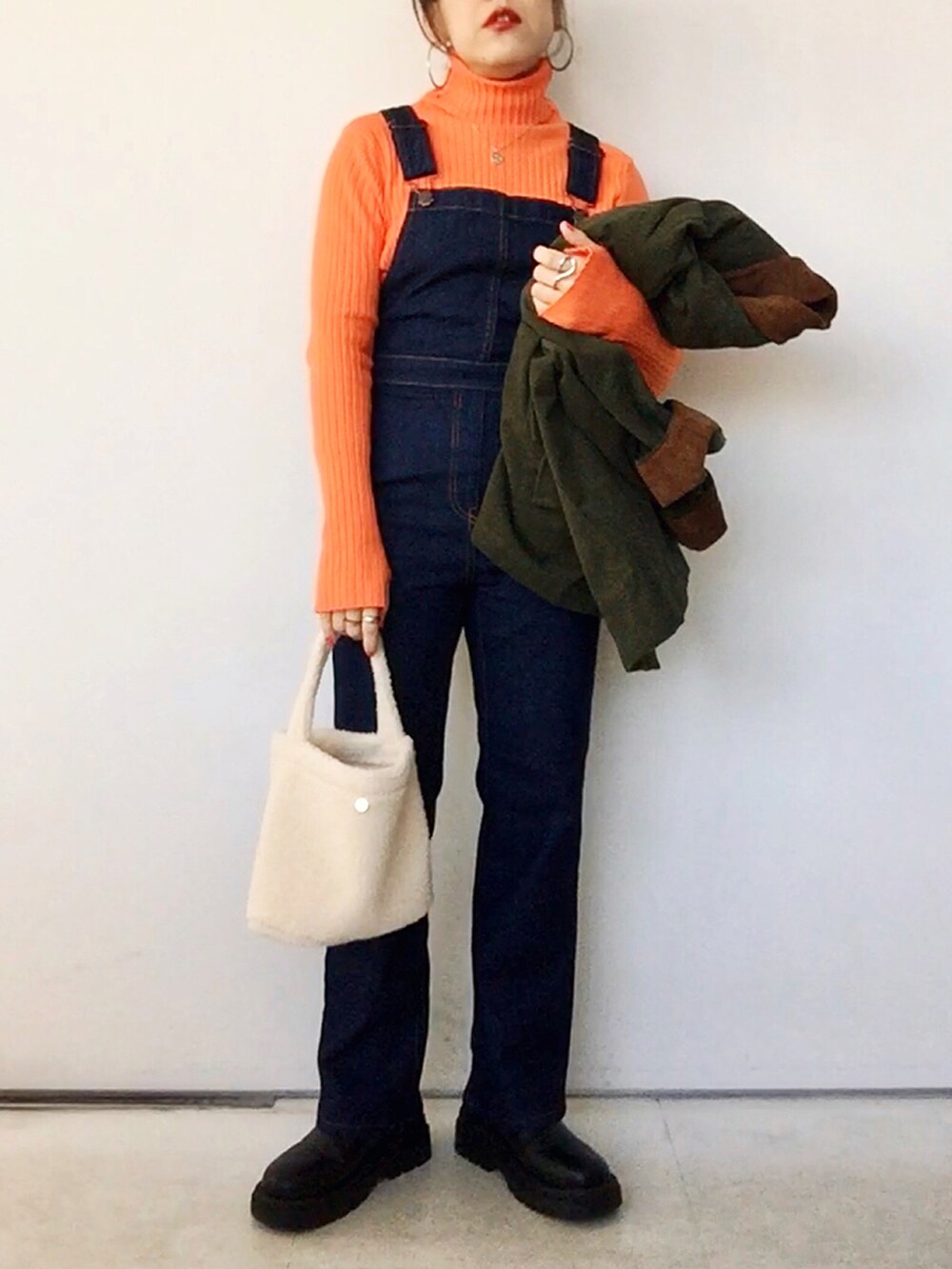 オレンジ系のニット/セーター、グリーン系のジャケット/アウター、ブルー系のサロペット/オーバーオールを着用したレディースの冬コーディネートの4枚目の写真