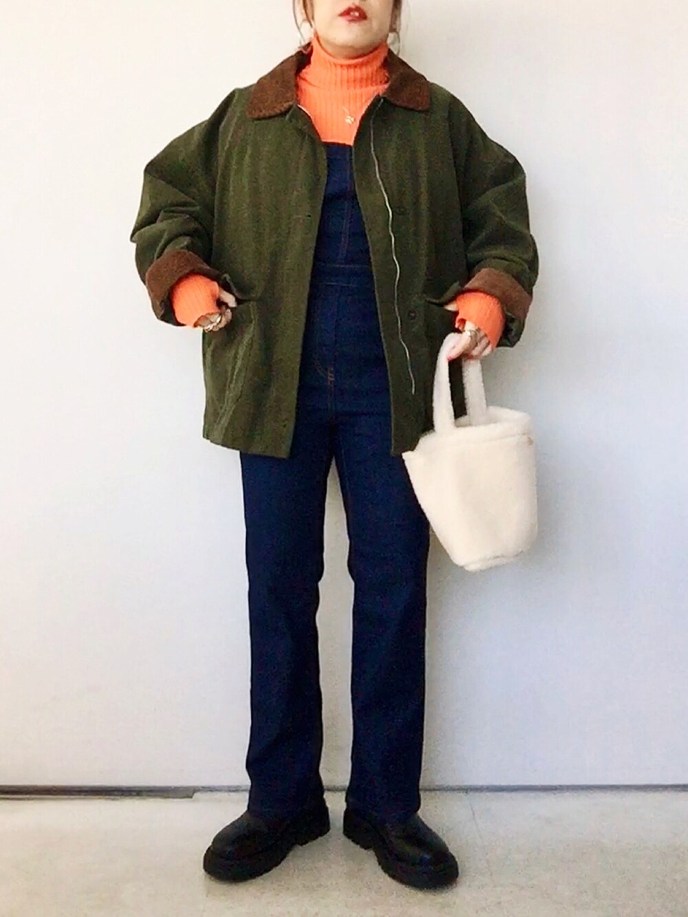 オレンジ系のニット/セーター、グリーン系のジャケット/アウター、ブルー系のサロペット/オーバーオールを着用したレディースの冬コーディネートの2枚目の写真