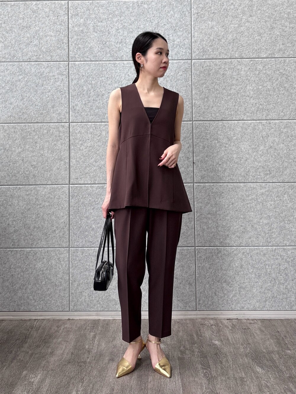 ブラック系のハンドバッグ、ブラウン系のベスト、ブラウン系のその他パンツを着用したレディースの秋コーディネートの2枚目の写真