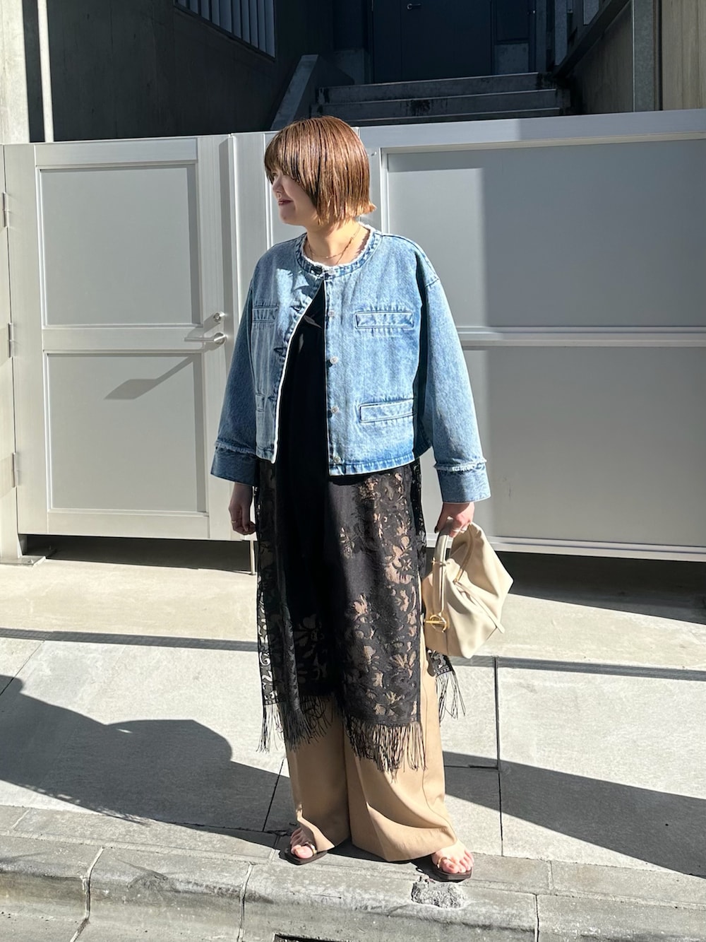 ブルー系のデニムジャケット、ブラック系のワンピース、ベージュ系のハンドバッグを着用したレディースの春コーディネートの2枚目の写真