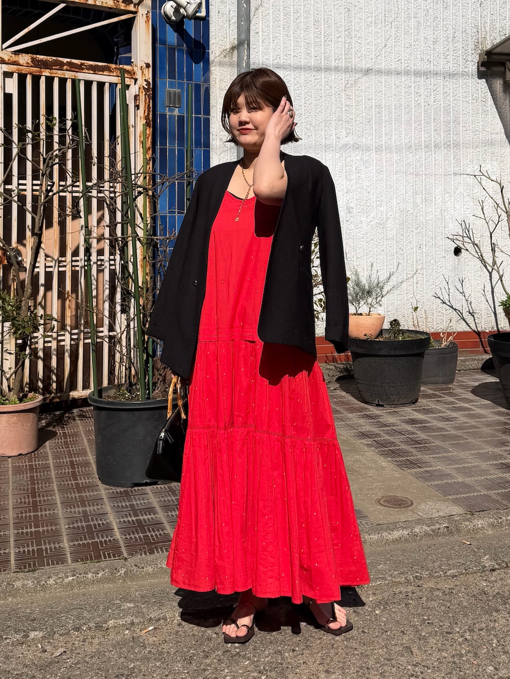 レッド系のワンピース、ブラック系のノーカラージャケット、ブラック系のハンドバッグを着用したレディースの春コーディネートの2枚目の写真