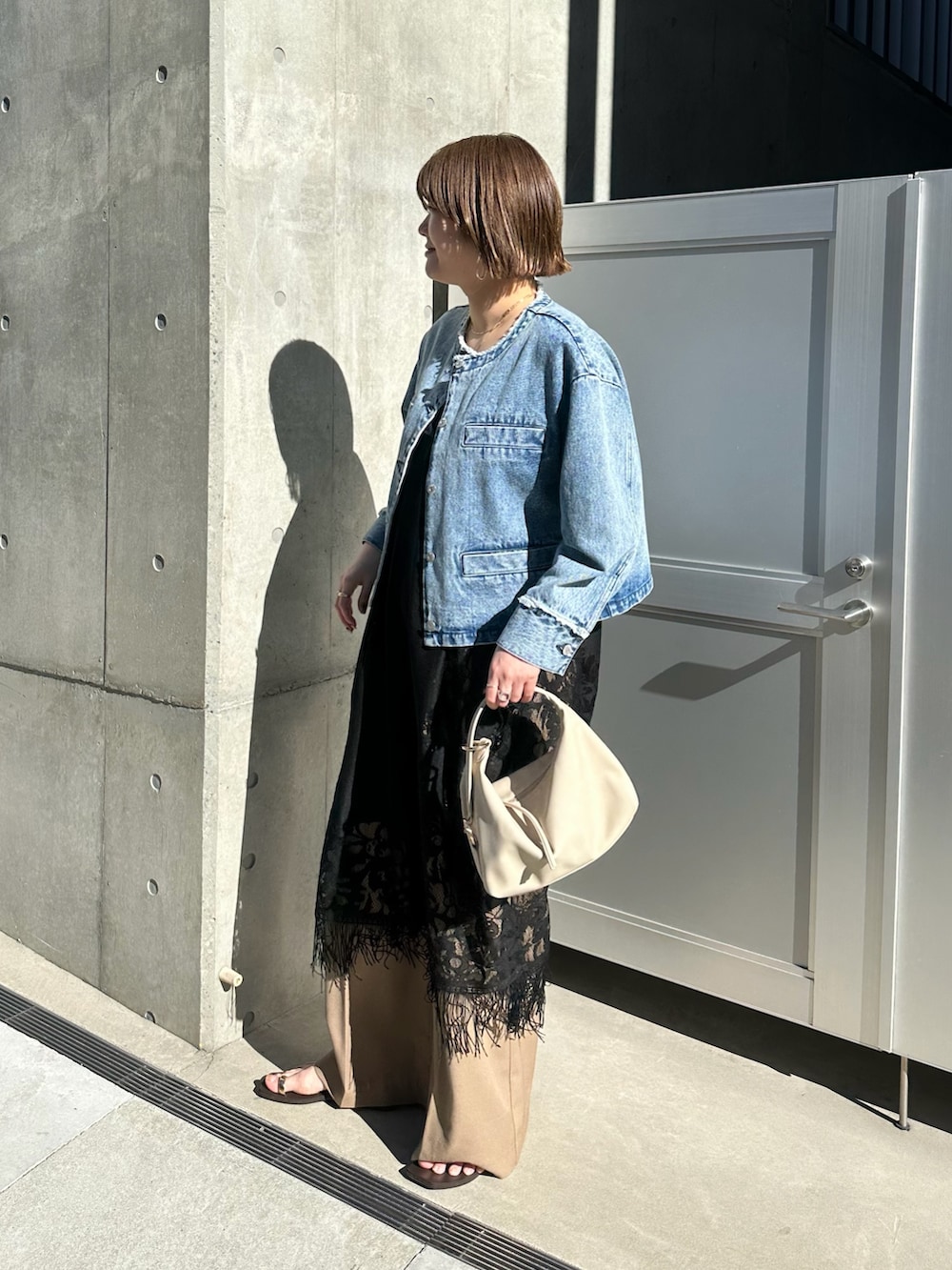 ブルー系のデニムジャケット、ブラック系のワンピース、ベージュ系のハンドバッグを着用したレディースの春コーディネートの3枚目の写真