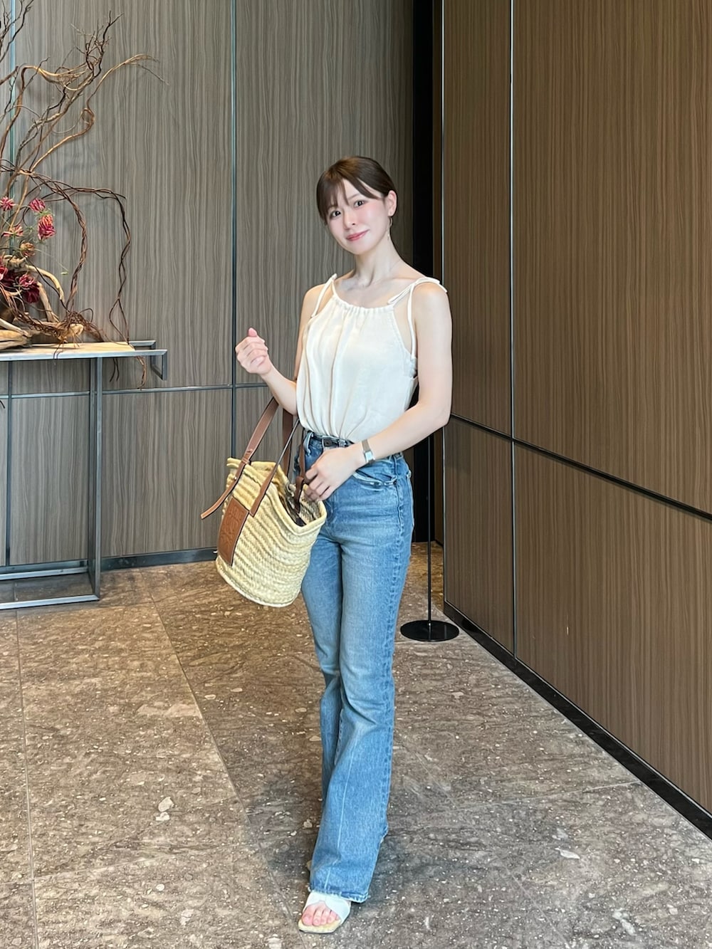 ブルー系のデニムパンツ、ベージュ系のかごバッグ、ホワイト系のサンダルを着用したレディースの夏コーディネートの2枚目の写真