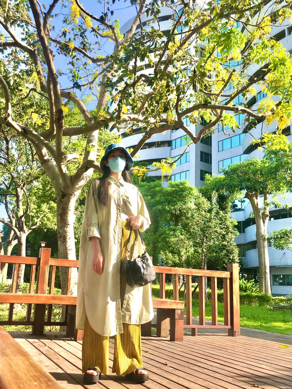 グリーン系のシャツワンピース、ゴールド系のパンツ、ブラック系のバッグを着用したレディースの春コーディネートの3枚目の写真