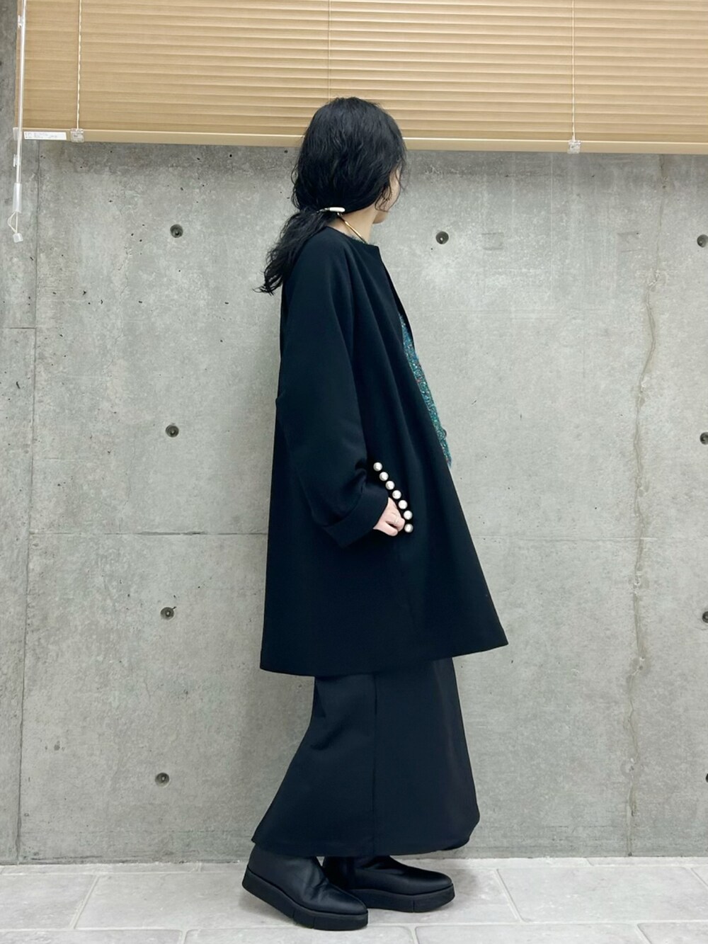ブラック系のノーカラーコート、ブルー系のニット/セーター、ブラック系のスカートを着用したレディースの秋コーディネートの3枚目の写真