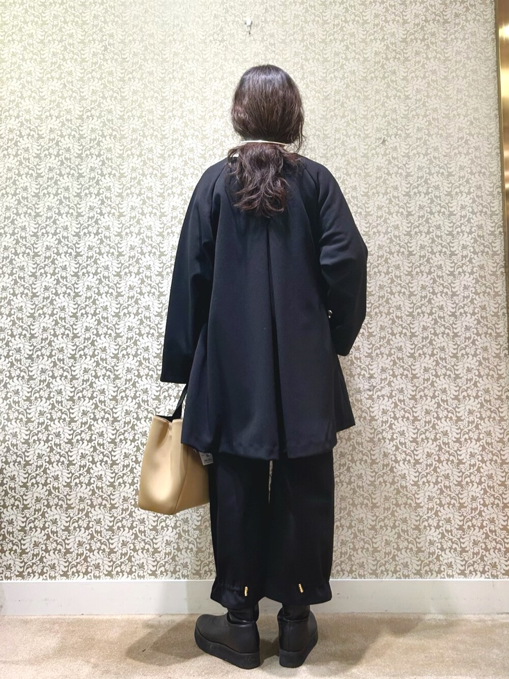 ブラック系のノーカラーコート、ベージュ系のニット/セーター、ブラック系のその他パンツを着用したレディースの冬コーディネートの2枚目の写真