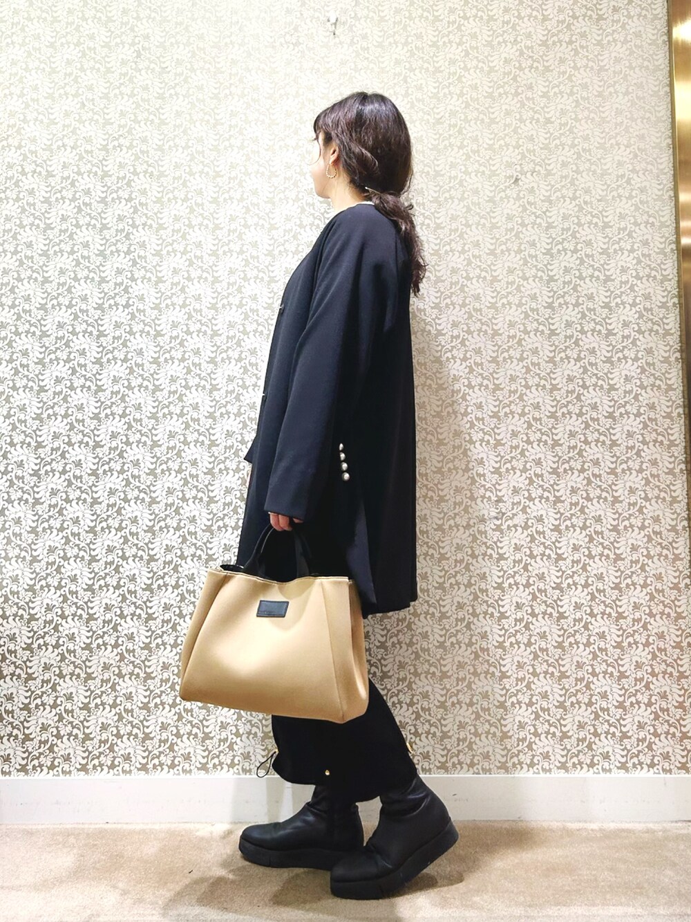 ブラック系のノーカラーコート、ベージュ系のニット/セーター、ブラック系のその他パンツを着用したレディースの冬コーディネートの3枚目の写真