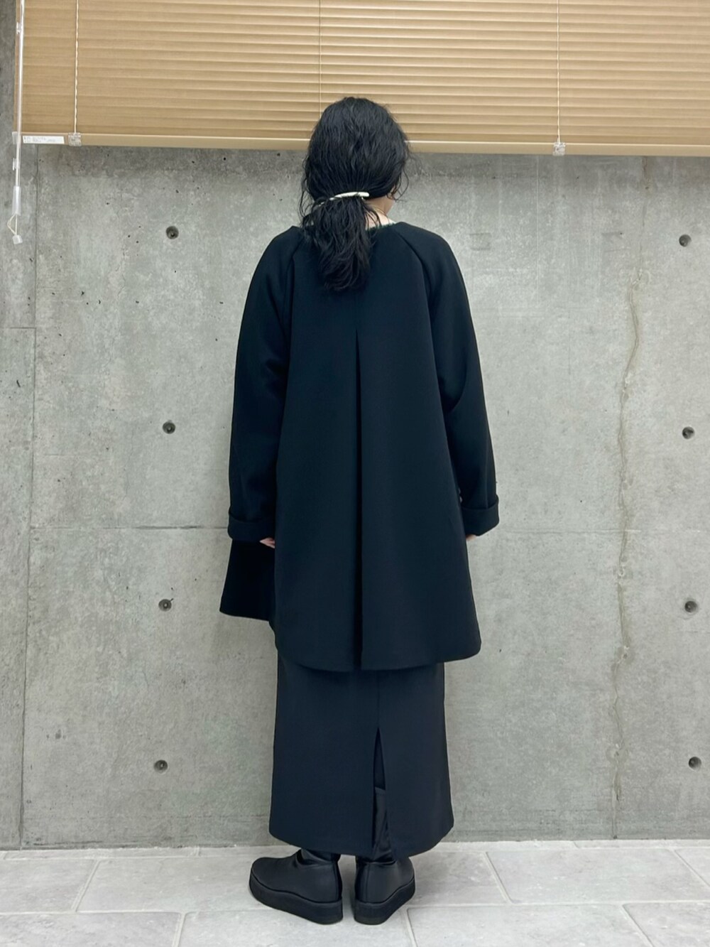 ブラック系のノーカラーコート、ブルー系のニット/セーター、ブラック系のスカートを着用したレディースの秋コーディネートの4枚目の写真