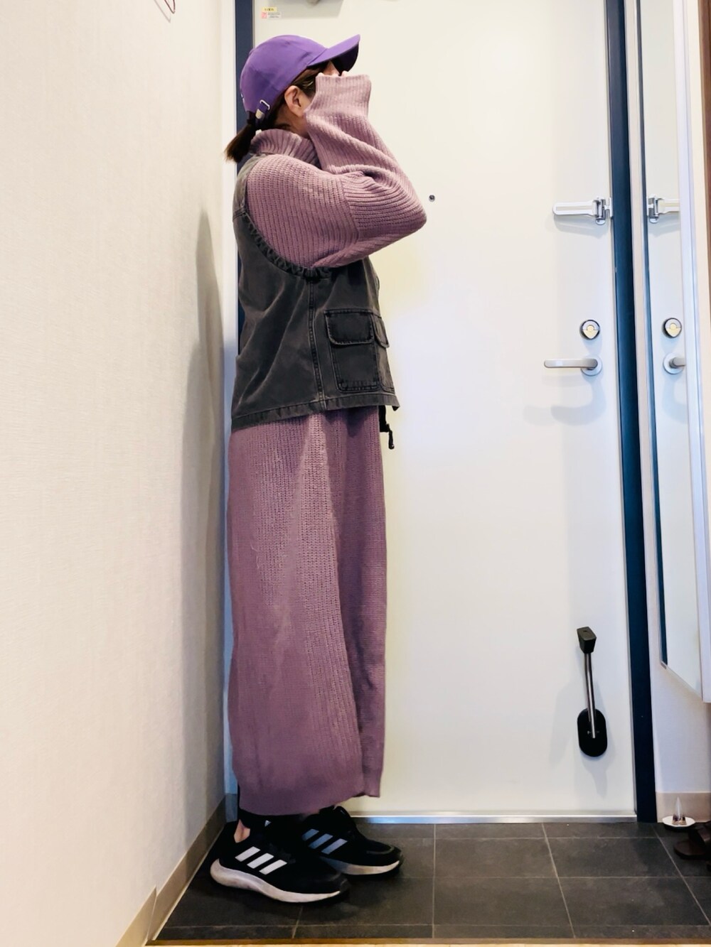 パープル系のワンピース、ブラック系のベスト、ブラック系のスニーカーを着用したレディースの秋コーディネートの2枚目の写真