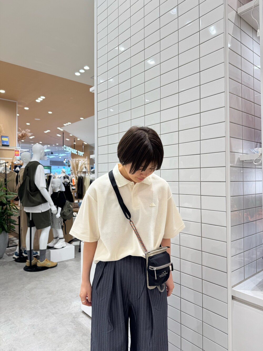 グレー系のスラックス、ホワイト系のポロシャツ、ベージュ系のショルダーバッグを着用したレディースの夏コーディネートの4枚目の写真