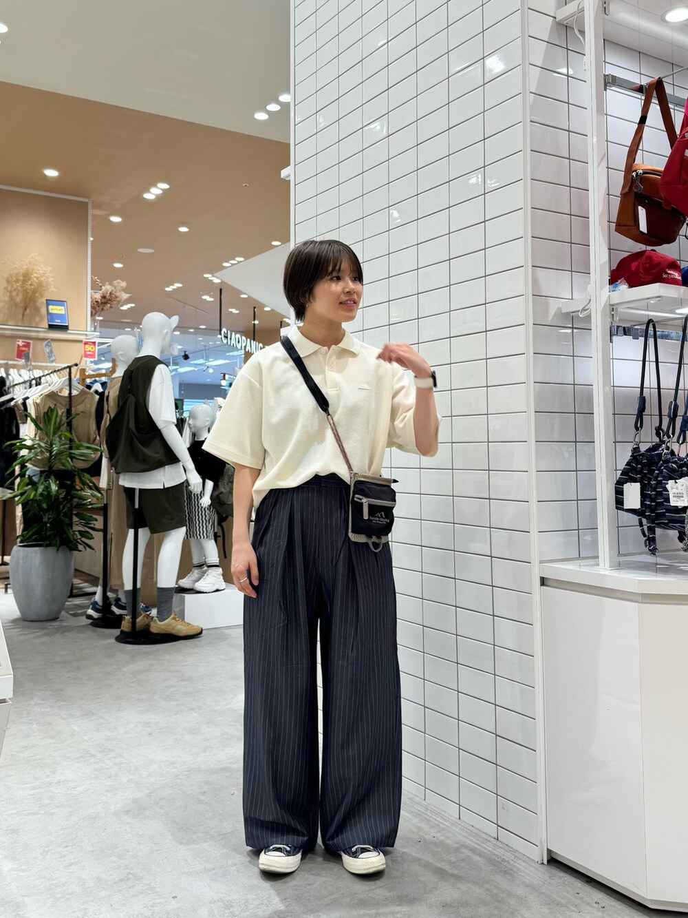 グレー系のスラックス、ホワイト系のポロシャツ、ベージュ系のショルダーバッグを着用したレディースの夏コーディネートの2枚目の写真